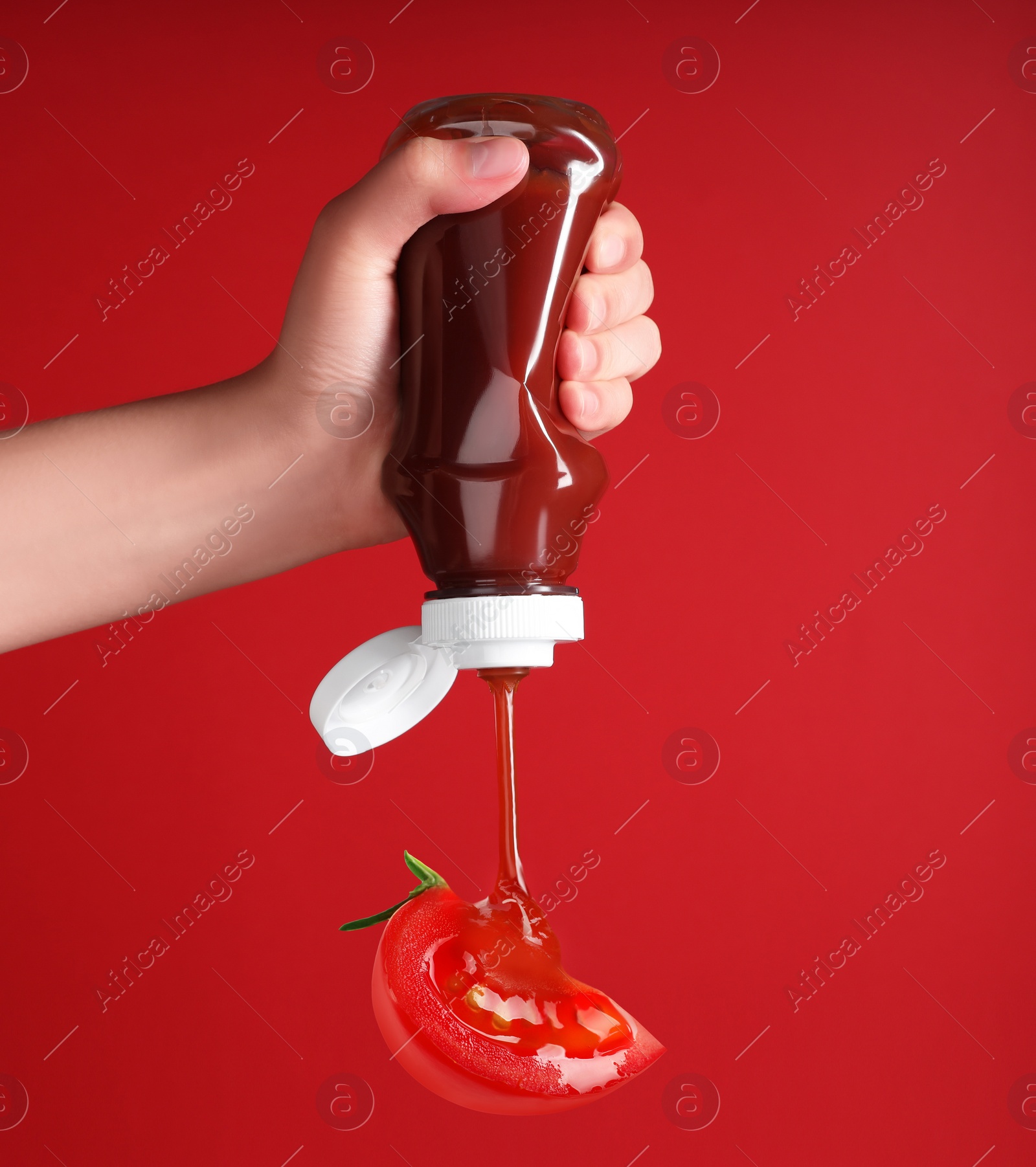 Image of Woman squeezing organic ketchup onto cut tomato against red background, closeup