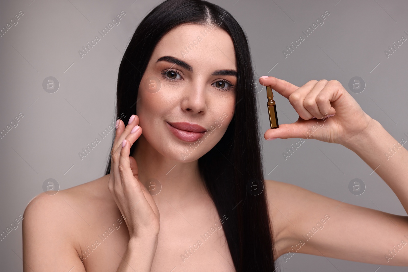 Photo of Beautiful young woman holding skincare ampoule on grey background