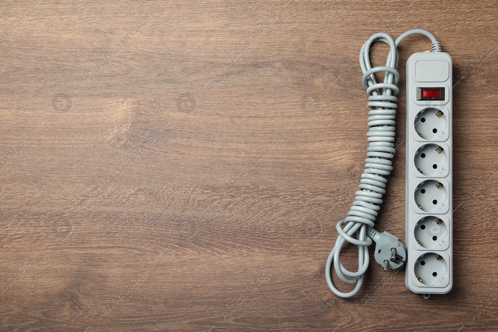 Photo of Power strip with extension cord on wooden floor, top view. Space for text