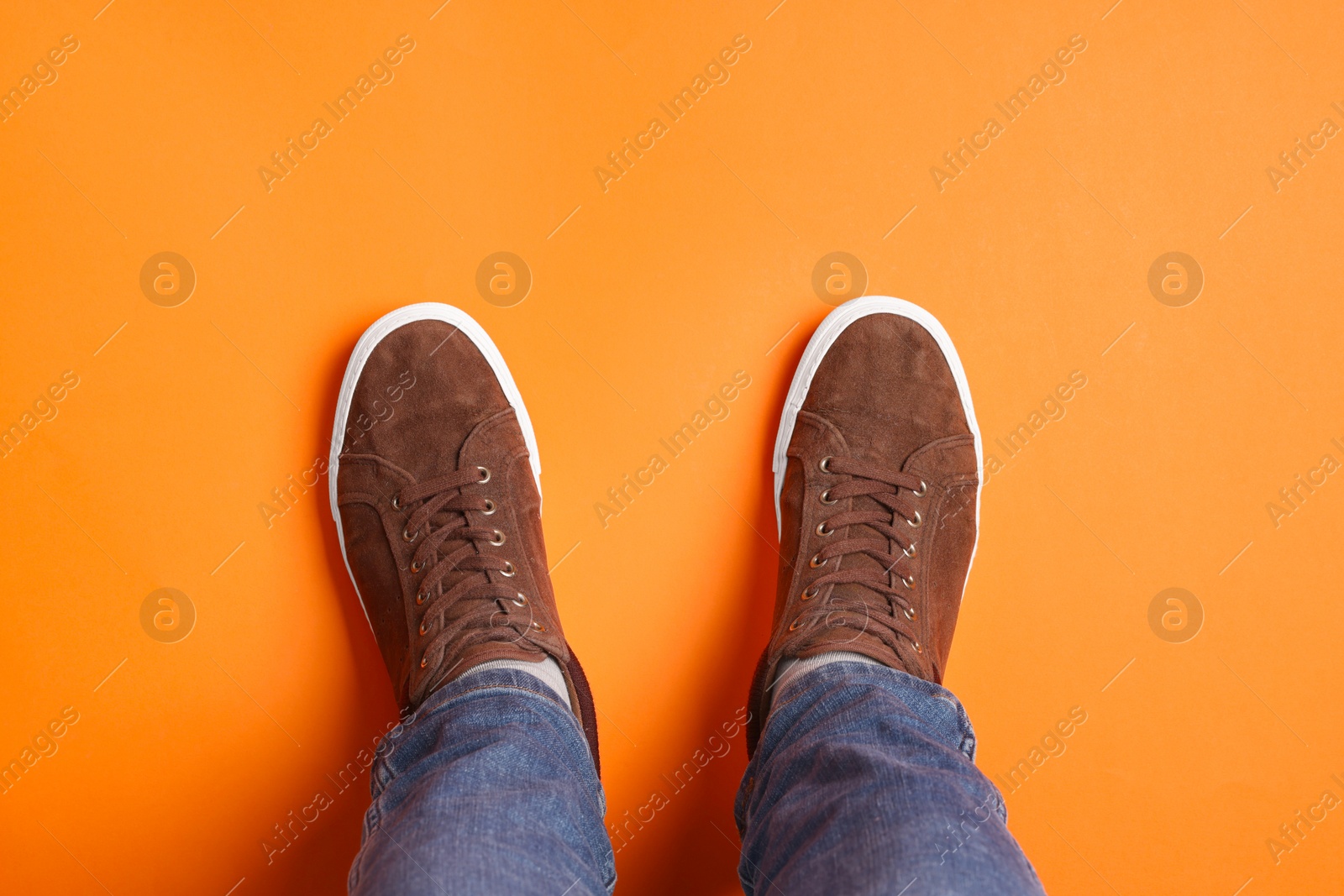 Photo of Man in stylish sneakers standing on orange background, top view