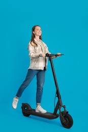 Happy woman riding modern electric kick scooter on light blue background