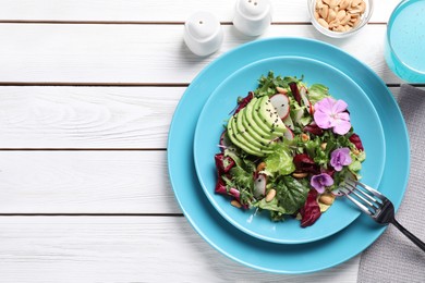 Fresh spring salad with flowers served on white wooden table, flat lay. Space for text