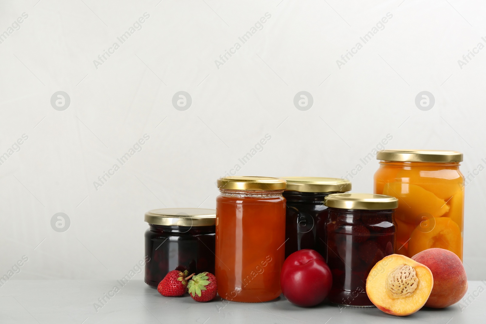 Photo of Jars of pickled fruits and jams on light table. Space for text