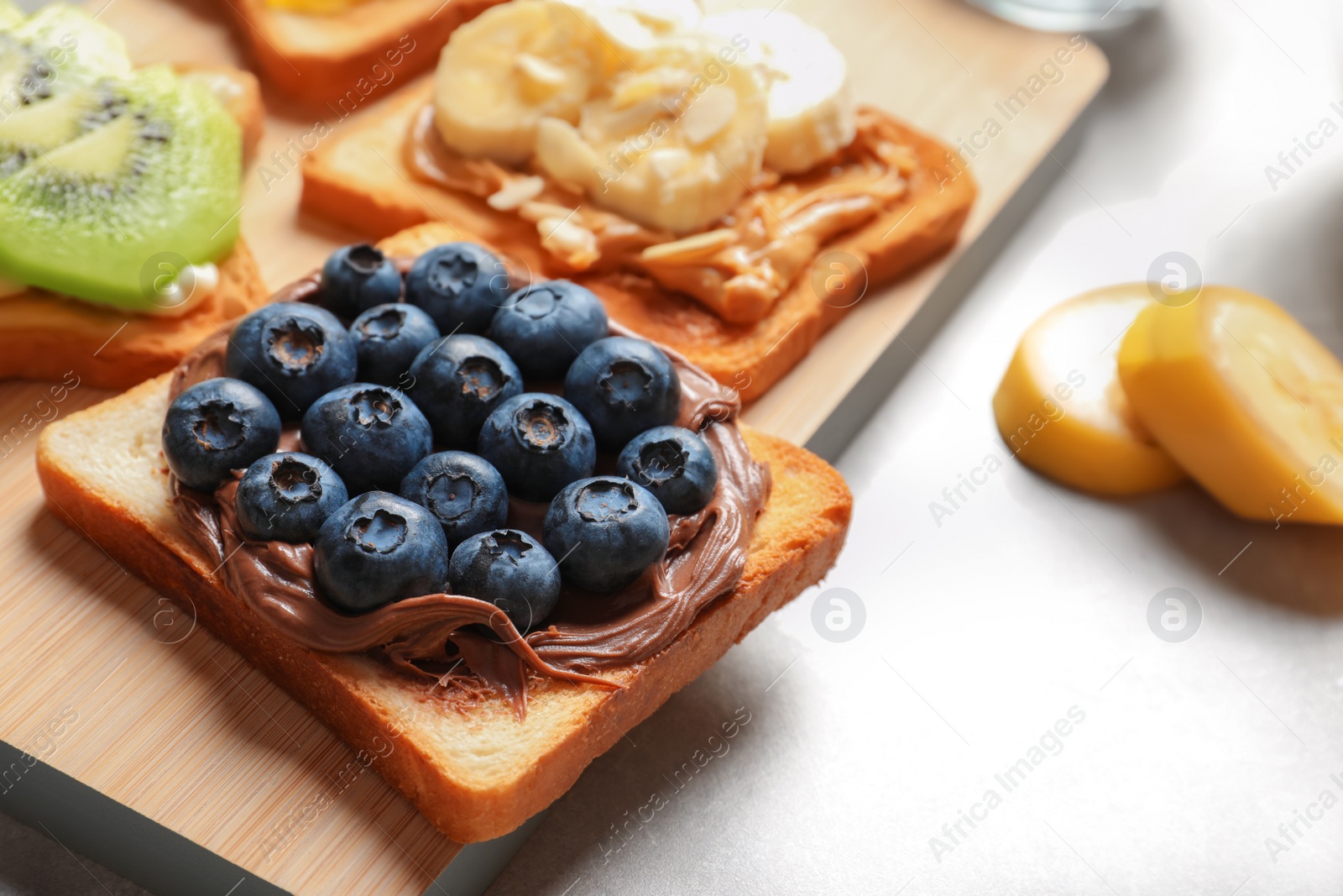 Photo of Toast bread with blueberries and chocolate paste on wooden board, closeup