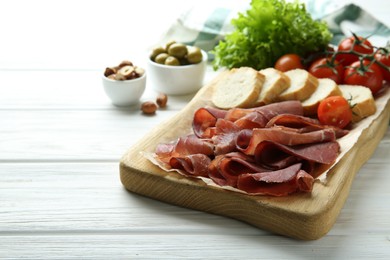 Photo of Board with delicious bresaola served with bread and tomato on white wooden table. Space for text