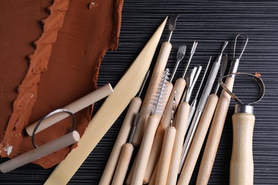 Clay and set of modeling tools on dark gray wooden table, flat lay