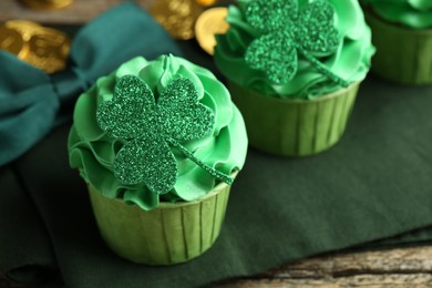 Photo of St. Patrick's day party. Tasty cupcakes with clover leaf toppers and green cream on wooden table, closeup