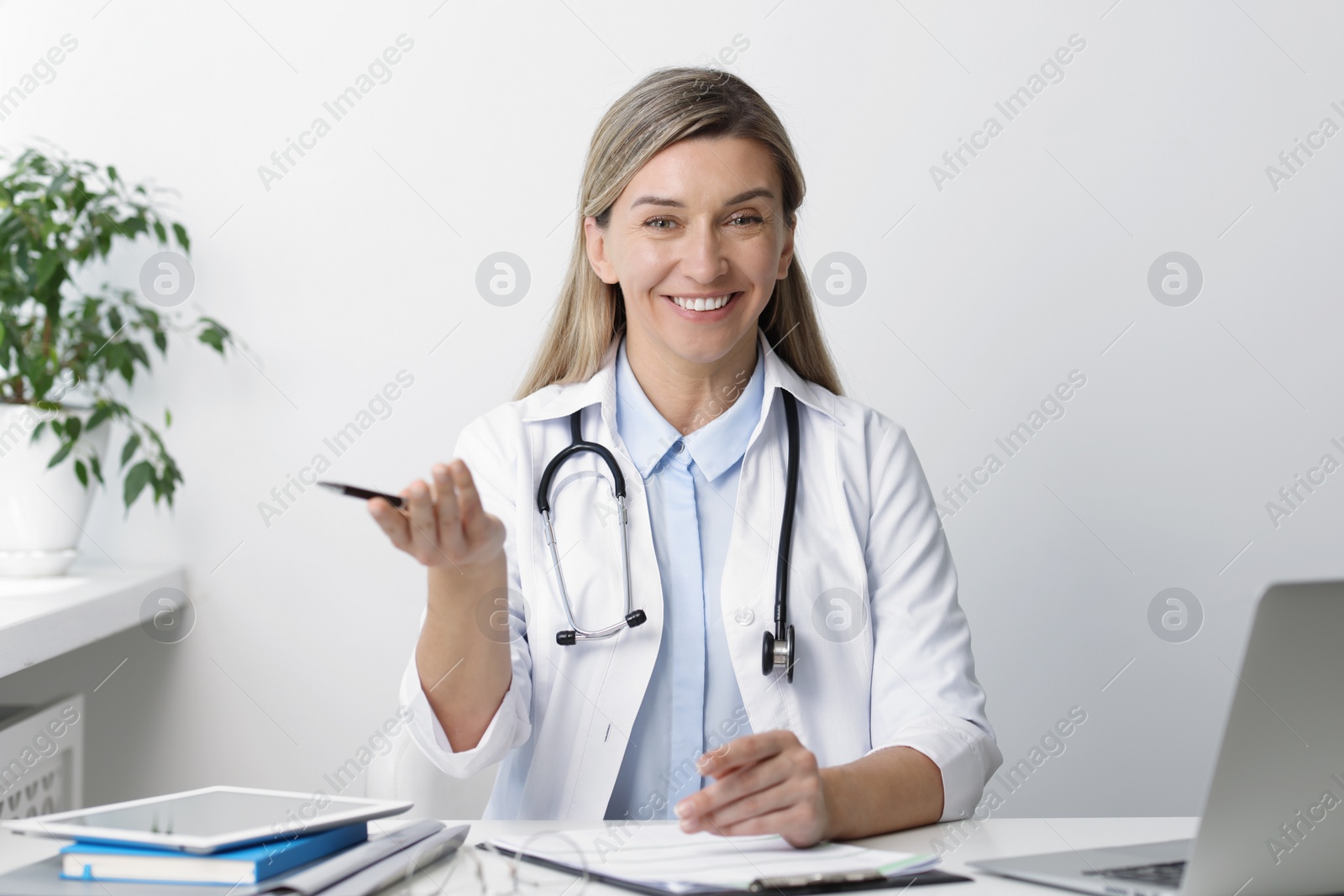 Photo of Portrait of happy doctor with stethoscope at white table in hospital