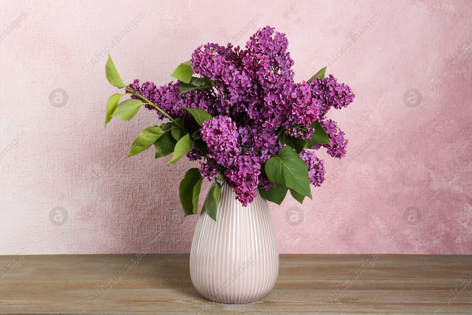 Photo of Beautiful lilac flowers in vase on wooden table