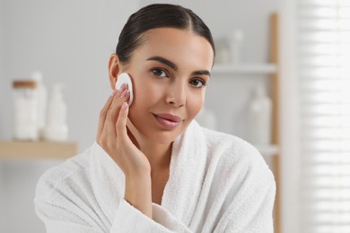 Beautiful woman removing makeup with cotton pad indoors