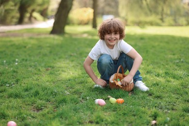 Easter celebration. Cute little boy hunting eggs outdoors, space for text