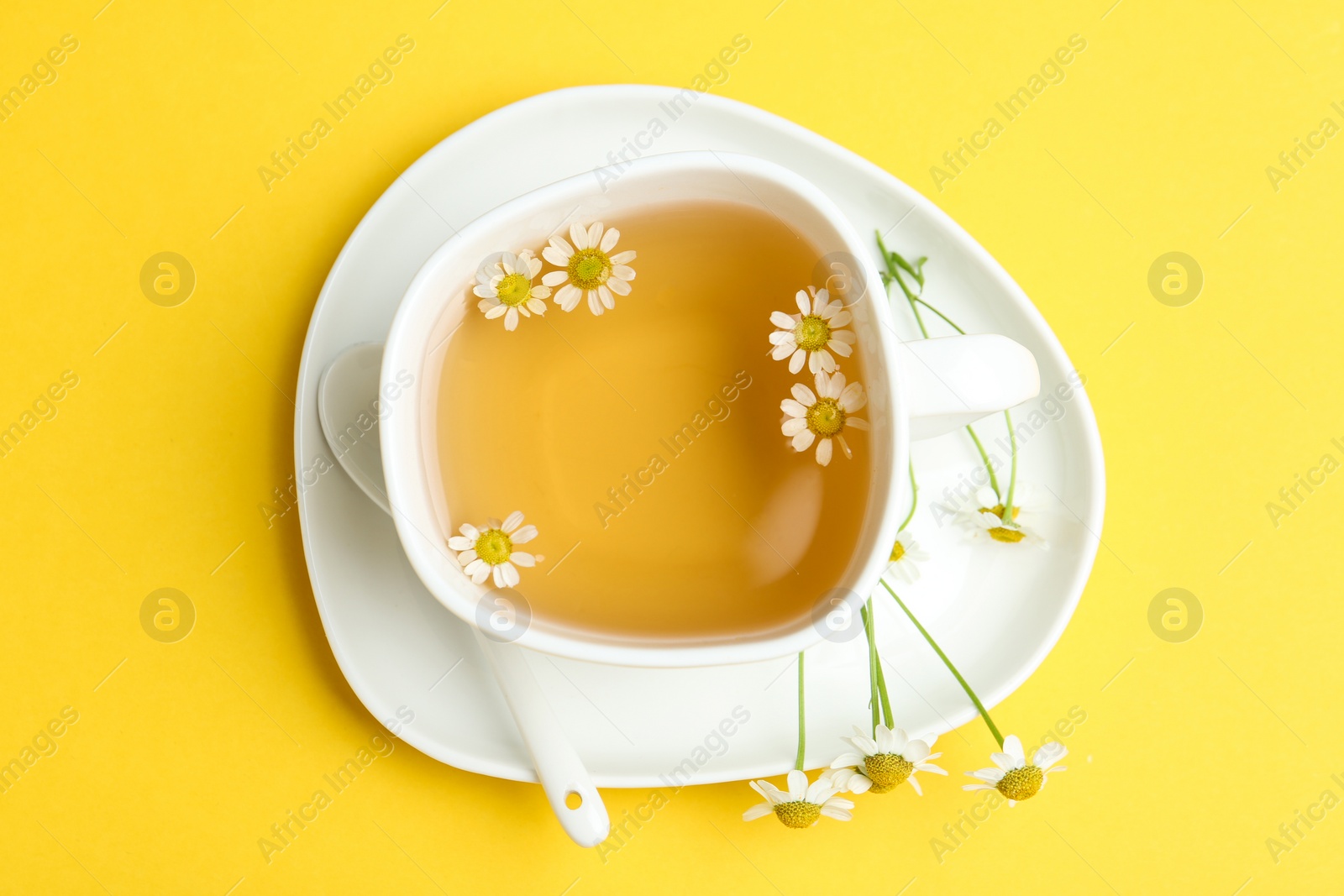 Photo of Delicious chamomile tea in cup on yellow background, top view