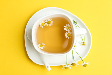 Photo of Delicious chamomile tea in cup on yellow background, top view