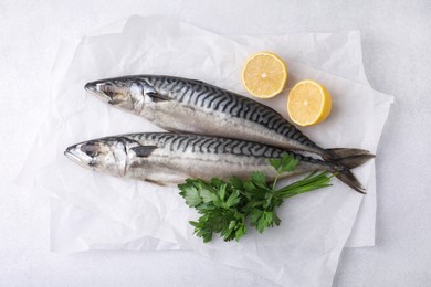 Photo of Tasty salted mackerels, parsley and cut lemons on light table, top view