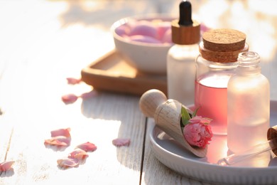 Bottles of rose essential oil and flowers on white wooden table, space for text