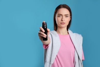 Young woman using pepper spray on light blue background