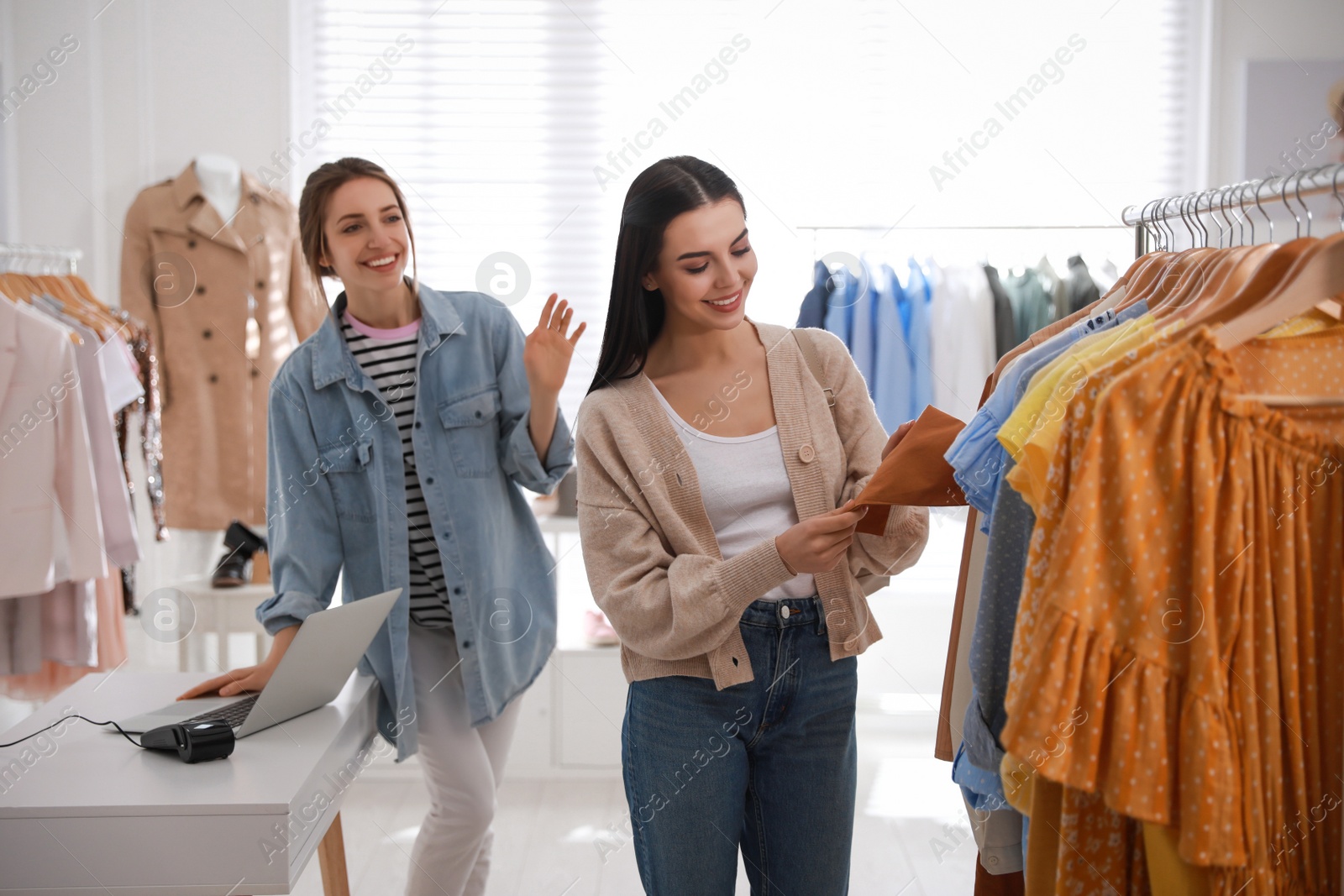 Photo of Shop assistant helping customer to choose clothes in modern boutique