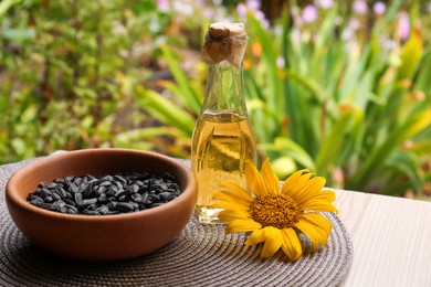 Bottle of sunflower oil and seeds in bowl on wooden table outdoors