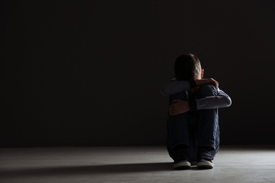 Photo of Upset boy sitting in dark room. Space for text