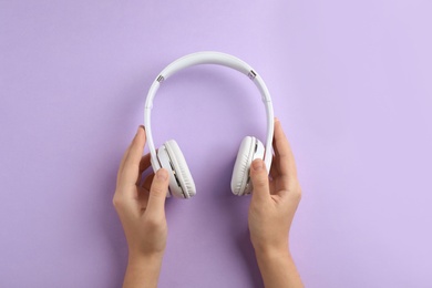 Woman holding headphones on color background, top view