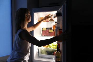 Woman taking sandwich out of refrigerator in kitchen at night