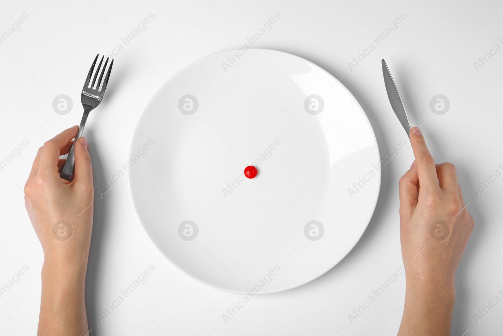 Photo of Woman holding cutlery near plate with weight loss pill on white background, top view