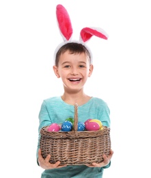 Photo of Little boy in bunny ears headband holding basket with Easter eggs on white background