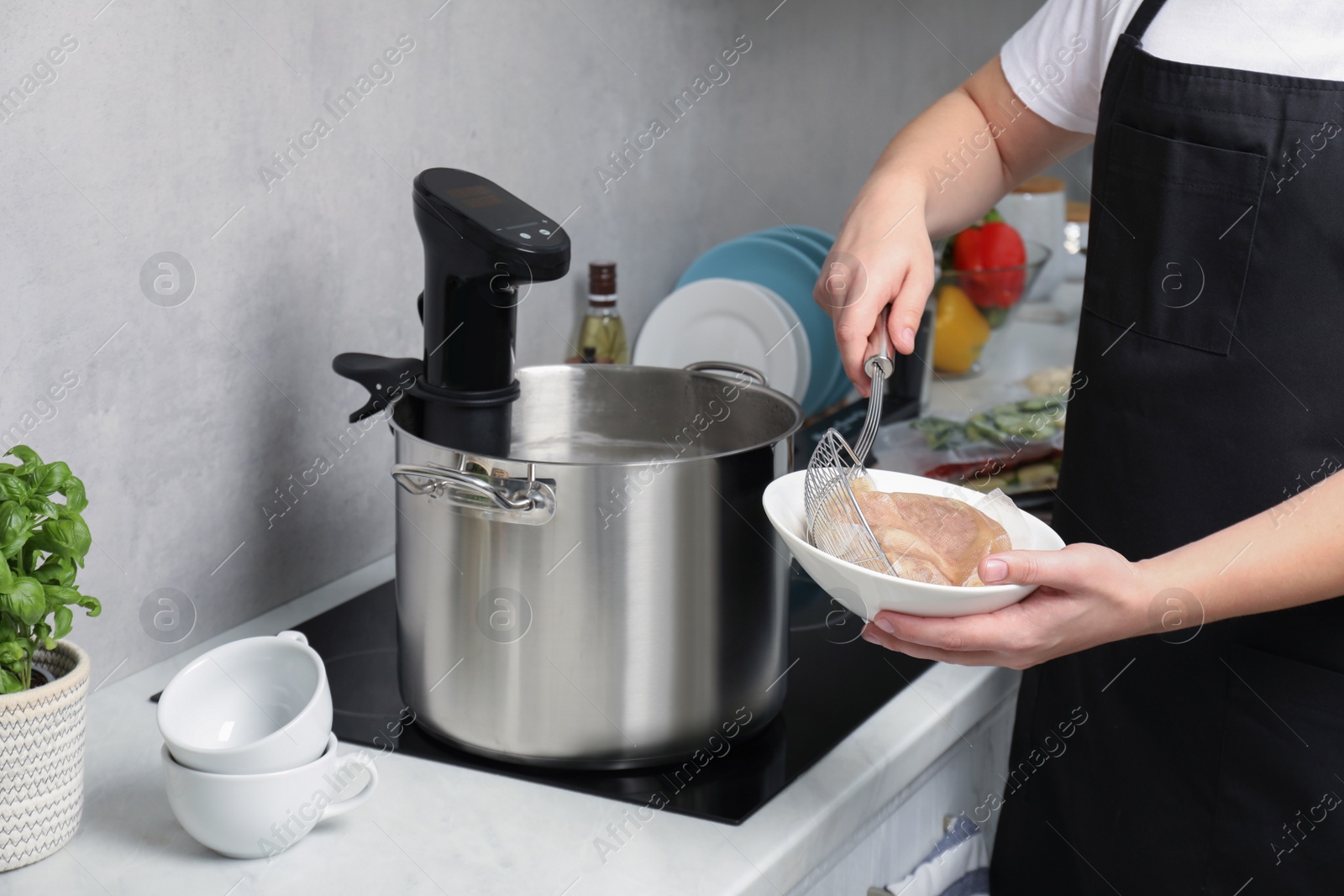 Photo of Woman taking out vacuum packed meat from pot in kitchen, closeup. Thermal immersion circulator for sous vide cooking