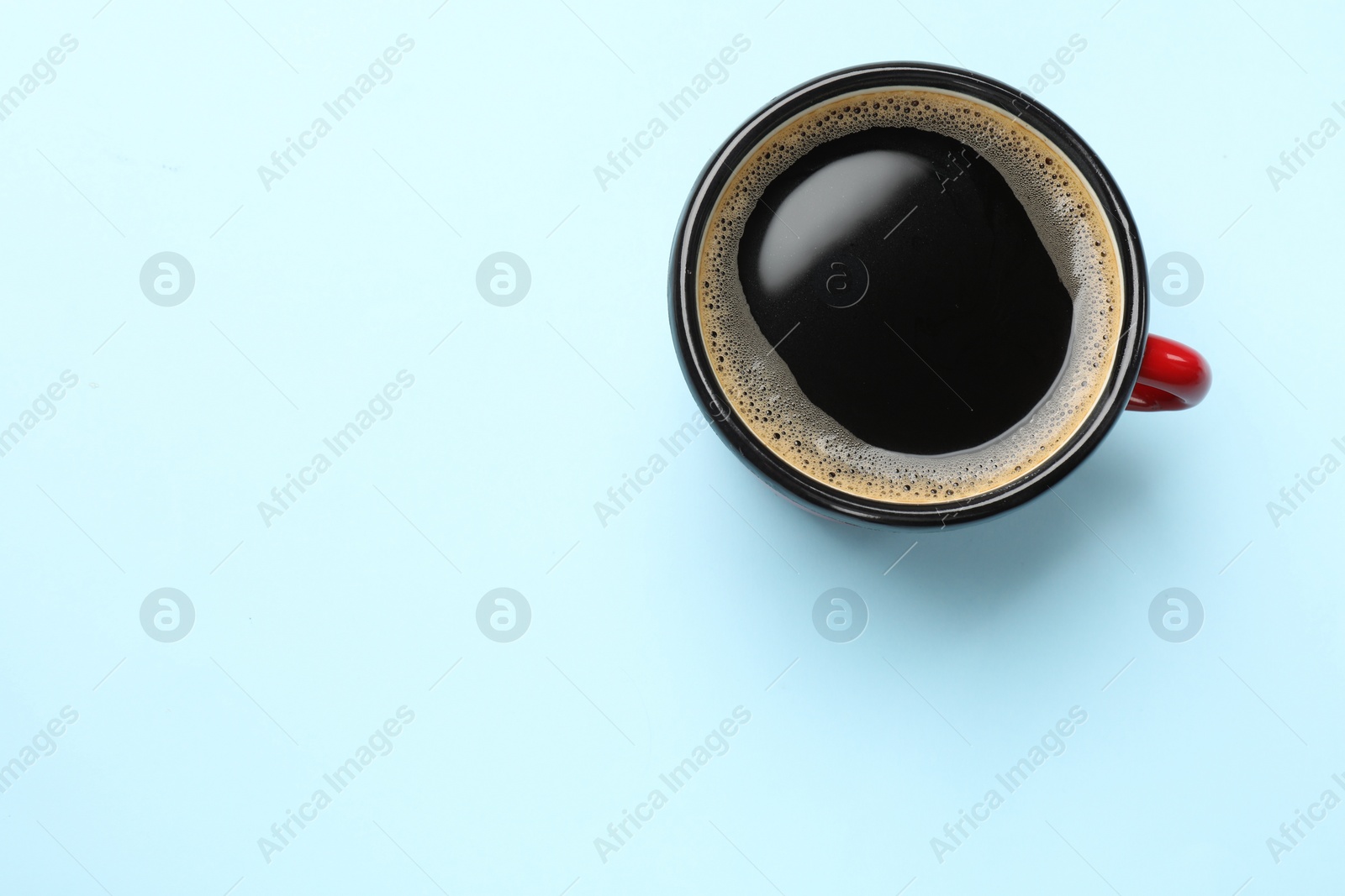 Photo of Aromatic coffee in cup on light blue background, top view. Space for text