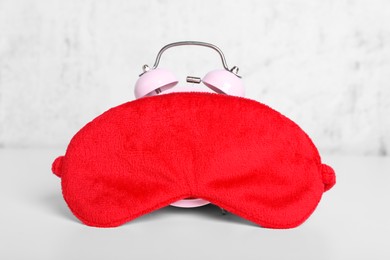 Photo of Red sleep mask and alarm clock on white table