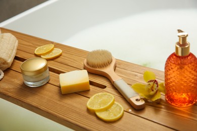 Photo of Wooden bath tray with bathroom amenities on tub, closeup