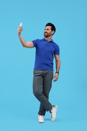 Photo of Smiling man taking selfie with smartphone on light blue background