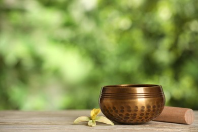 Photo of Golden singing bowl, mallet and flower on white wooden table outdoors, space for text