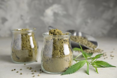 Hemp protein powder, seeds and fresh leaves on light grey table