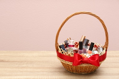 Wicker gift basket with cosmetic products on wooden table. Space for text