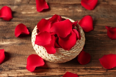 Wicker basket with rose petals on wooden background