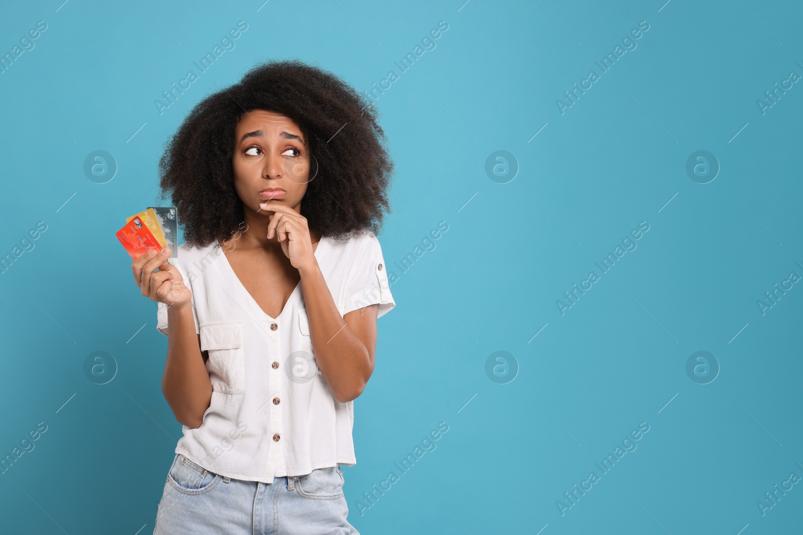 Photo of Confused woman with credit cards on light blue background, space for text. Debt problem