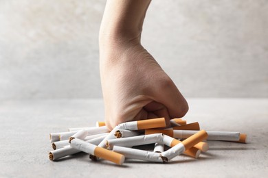 Photo of Stop smoking. Woman crushing cigarettes at grey table, closeup