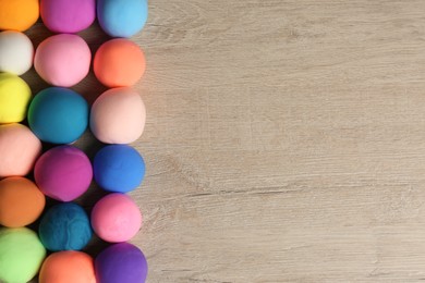 Different color play dough balls on wooden table, flat lay. Space for text