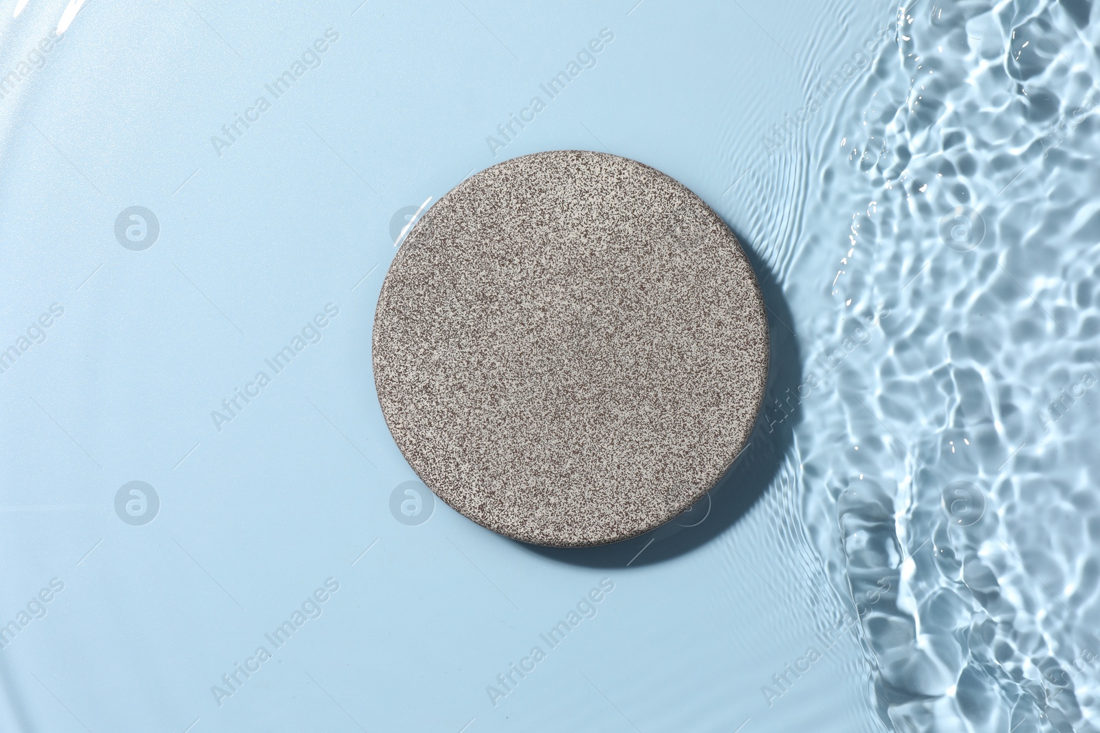 Photo of Presentation for product. Stone podium in water on light blue background, top view