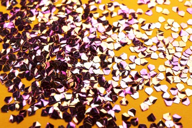 Photo of Shiny bright violet glitter on yellow background, closeup