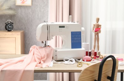 Photo of White sewing machine, cloth, craft accessories and mannequin on wooden table indoors