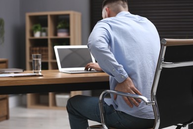 Photo of Man suffering from back pain while working with laptop in office. Symptom of poor posture