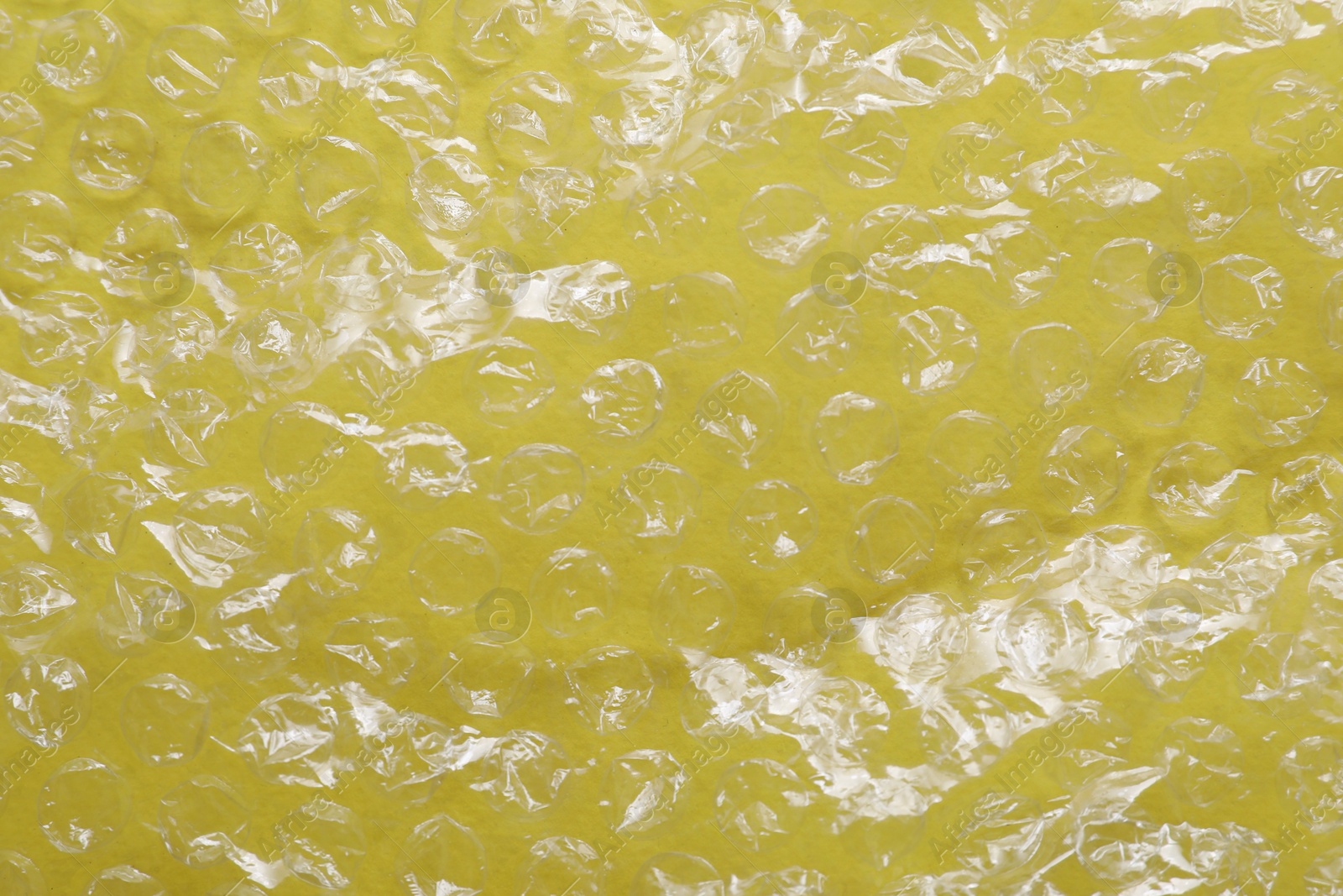 Photo of Transparent bubble wrap on yellow background, top view