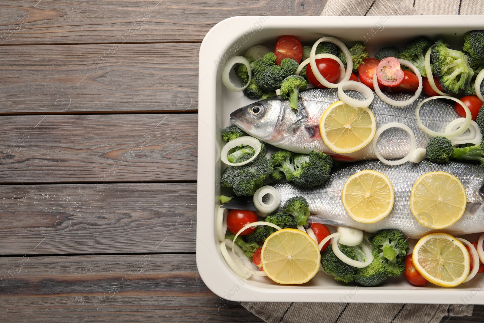 Photo of Raw fish with vegetables and lemon in baking dish on wooden table, top view. Space for text