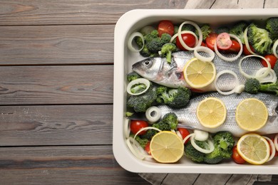 Photo of Raw fish with vegetables and lemon in baking dish on wooden table, top view. Space for text