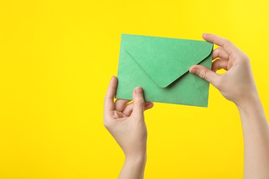 Photo of Woman holding green paper envelope on yellow background, closeup