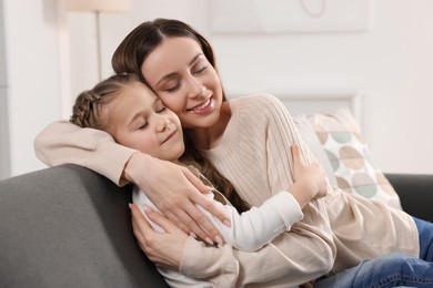 Photo of Happy mother hugging her cute daughter on sofa at home