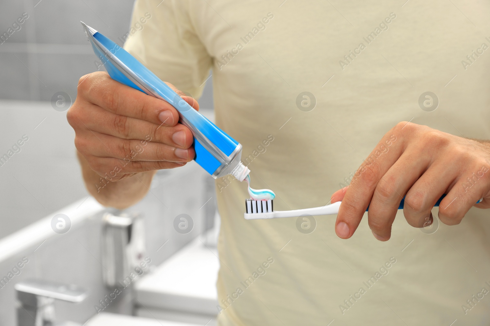 Photo of Man applying toothpaste on brush in bathroom, closeup