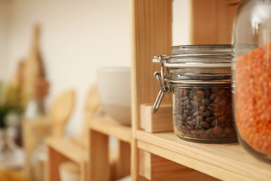 Glass jar with coffee beans on wooden shelf in kitchen, space for text